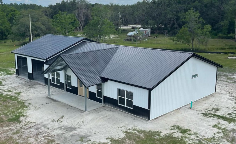 Modern white steel barndominium with black trim, standing seam metal roof, and covered front porch on a spacious rural property.
